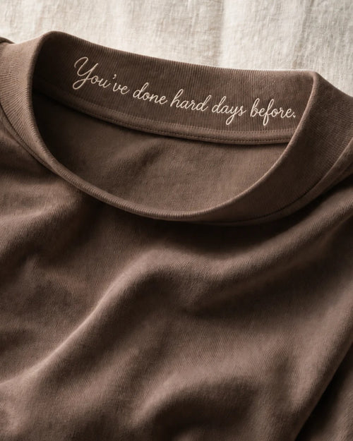 Close on the Mocha collar band, tipped forward: 'You've done hard days before.' embroidered in cream thread on the inner face, raised above the cloth.