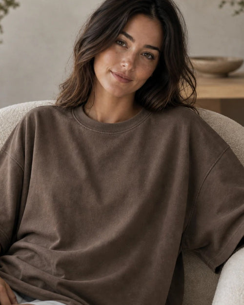 The oversized tee in Mocha, worn in a bouclé chair. Nothing is printed on the outside.